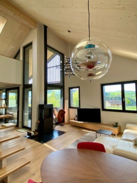 Large open-plan living and dining room with a modern fireplace, large windows and a view of the surrounding mountains, a flat-screen TV, and a ceiling lamp