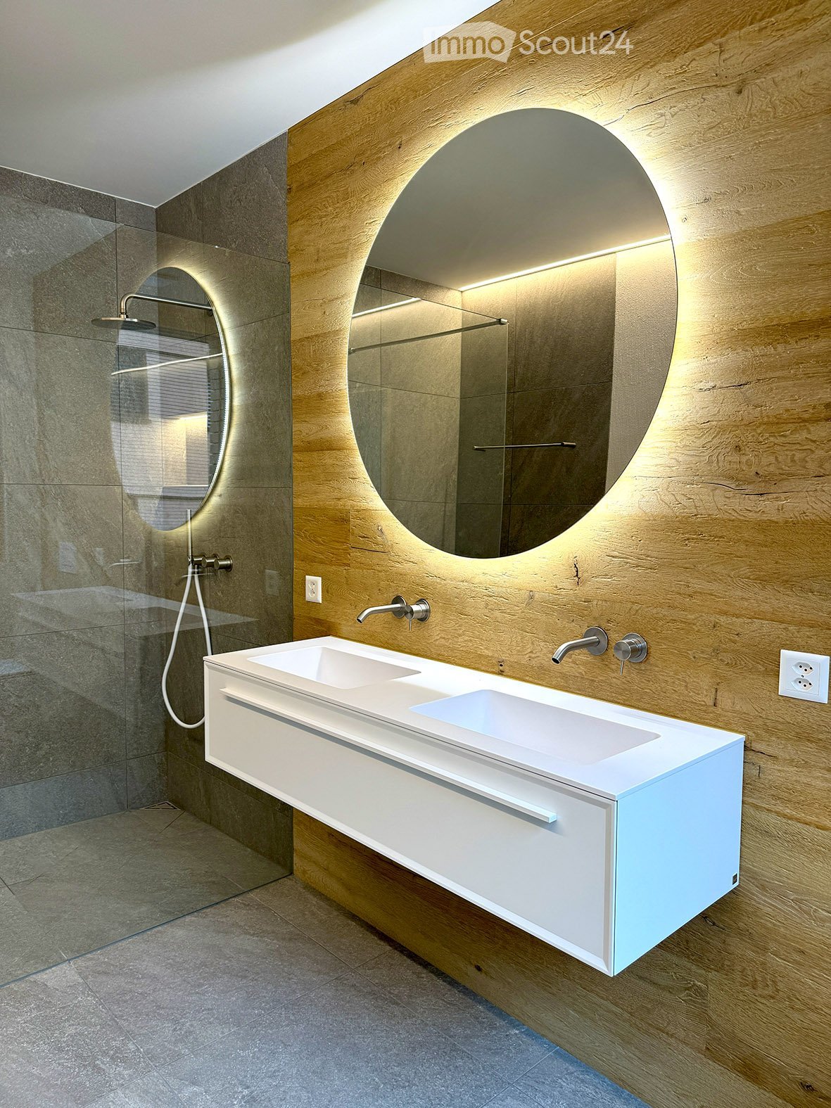 modern bathroom, with glass wall shower, large mirror, white counter top, double sinks, wooden walls, under sink cabinet