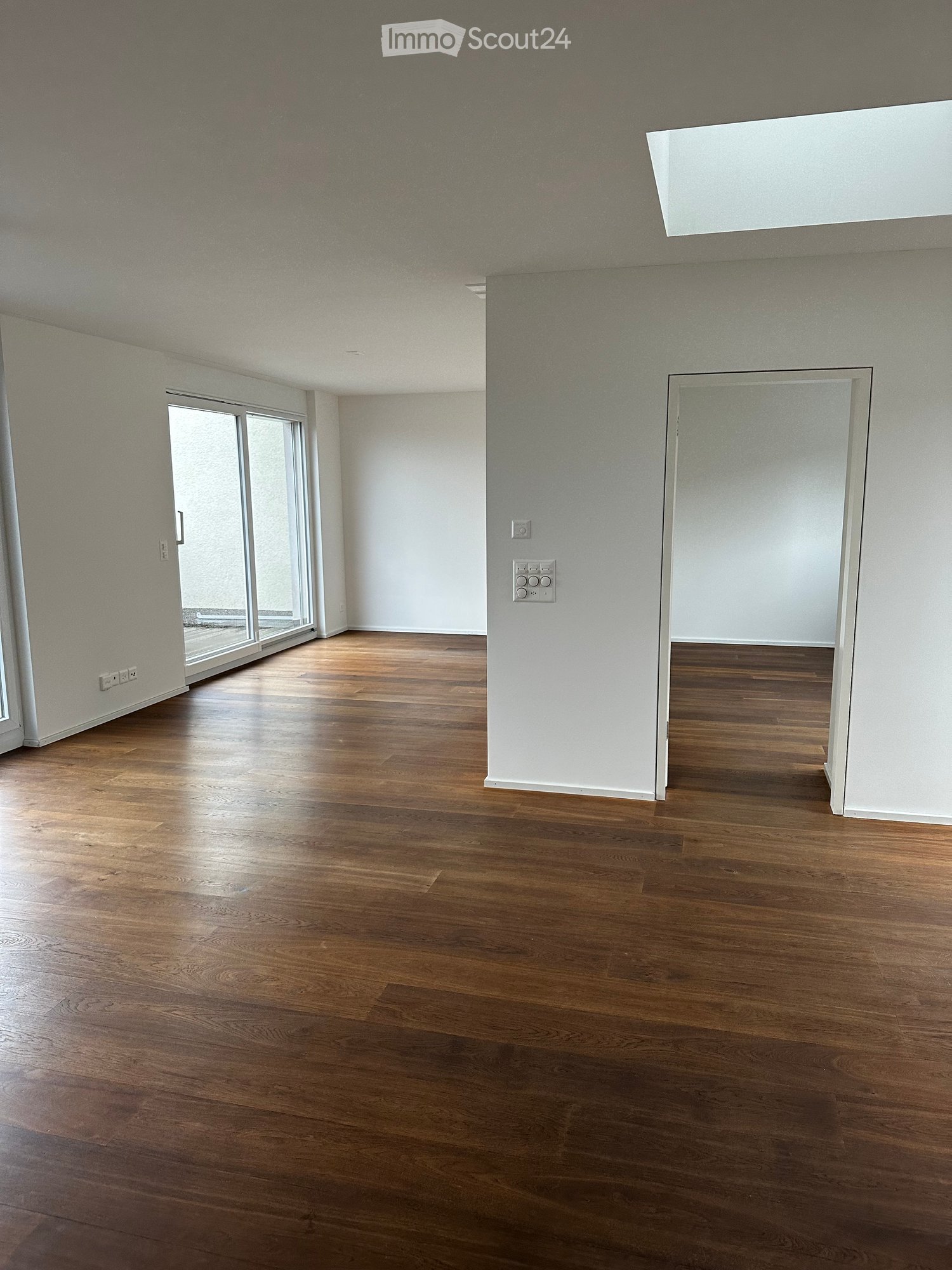 wide empty room, wooden floor, sliding doors leading to balcony, white walls, white ceiling, no furniture