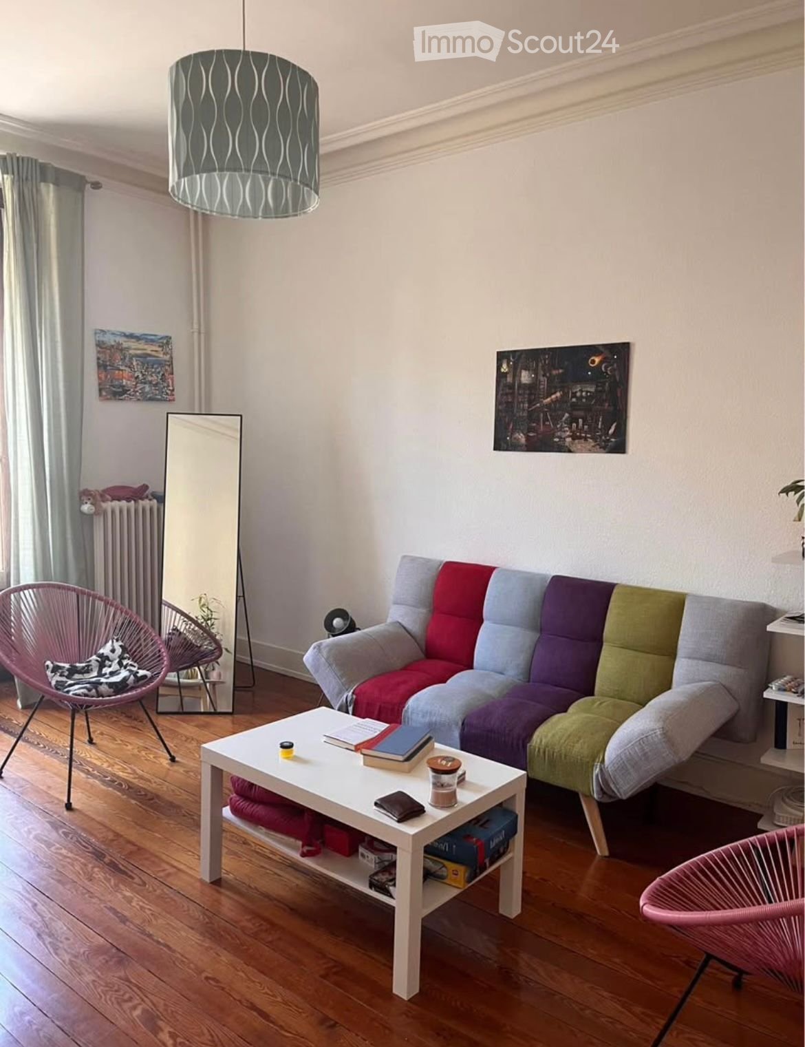 Living room: Multicolored couch, white coffee table, pink chairs, mirror, lamp