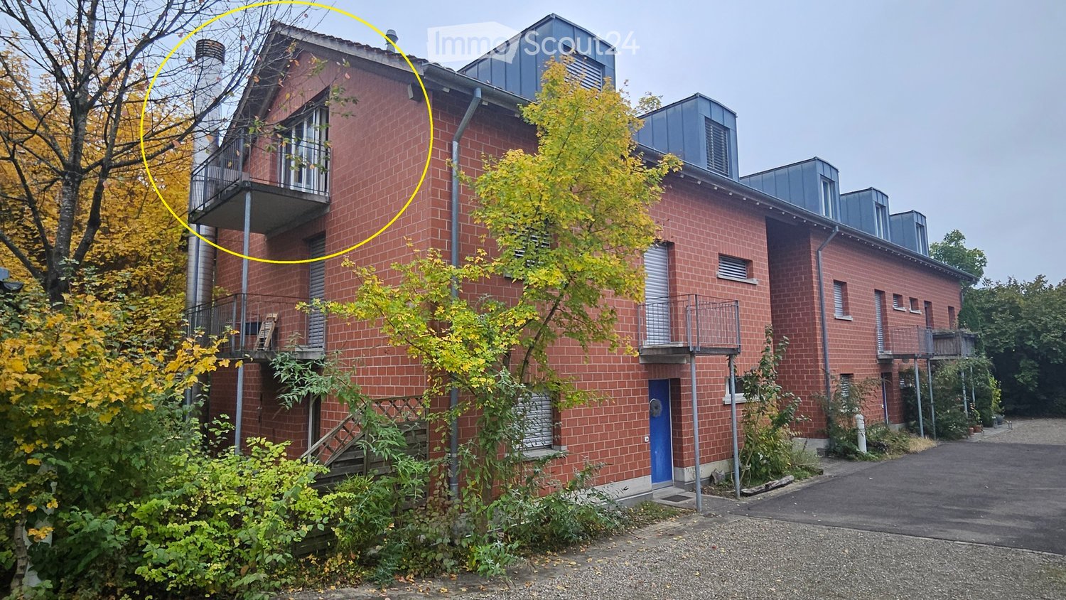 2 story brick building, blue door, balconies on the 1st floor, surrounded by plants and trees