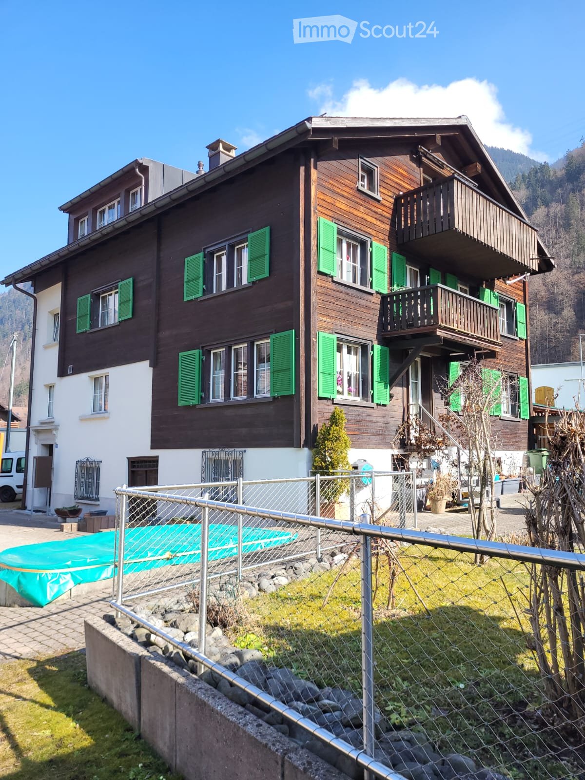 2 story building, brown wood, green shutters, balconies, garden, mountains in background