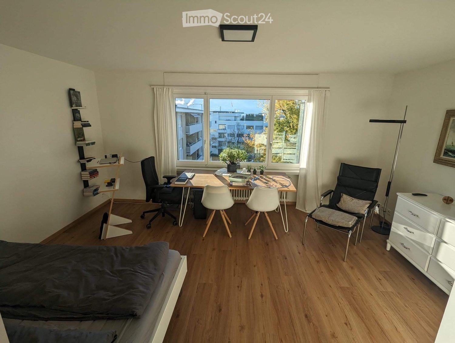modern room, wooden floor, white walls, window with white curtains, black office chair, wooden desk with black cushion, white arm chairs, black and white swivel chair, white dresser