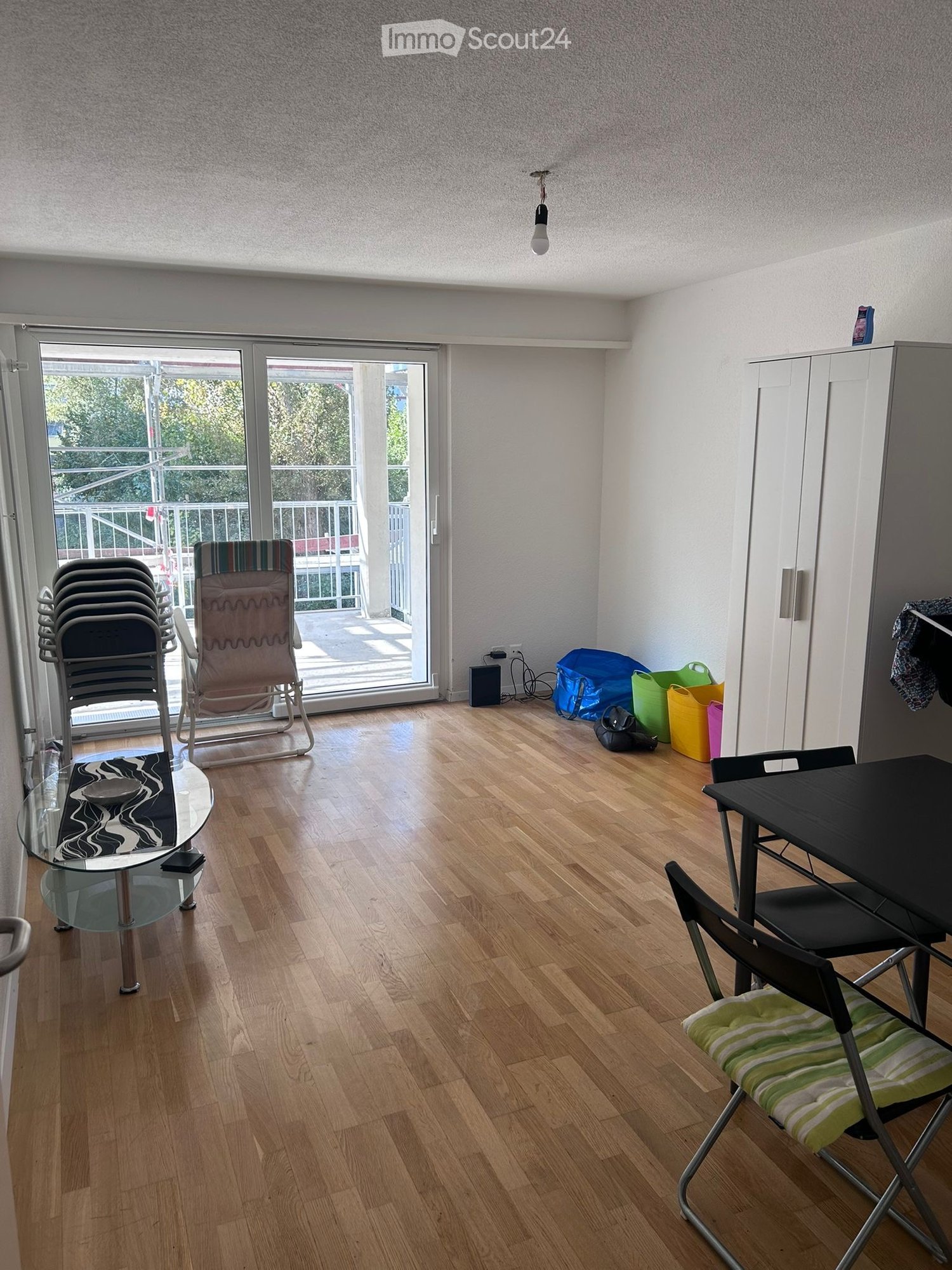 living room, wooden floor, large sliding glass door to balcony, glass table, folding chairs, chairs, side table, cupboard, hanging clothes