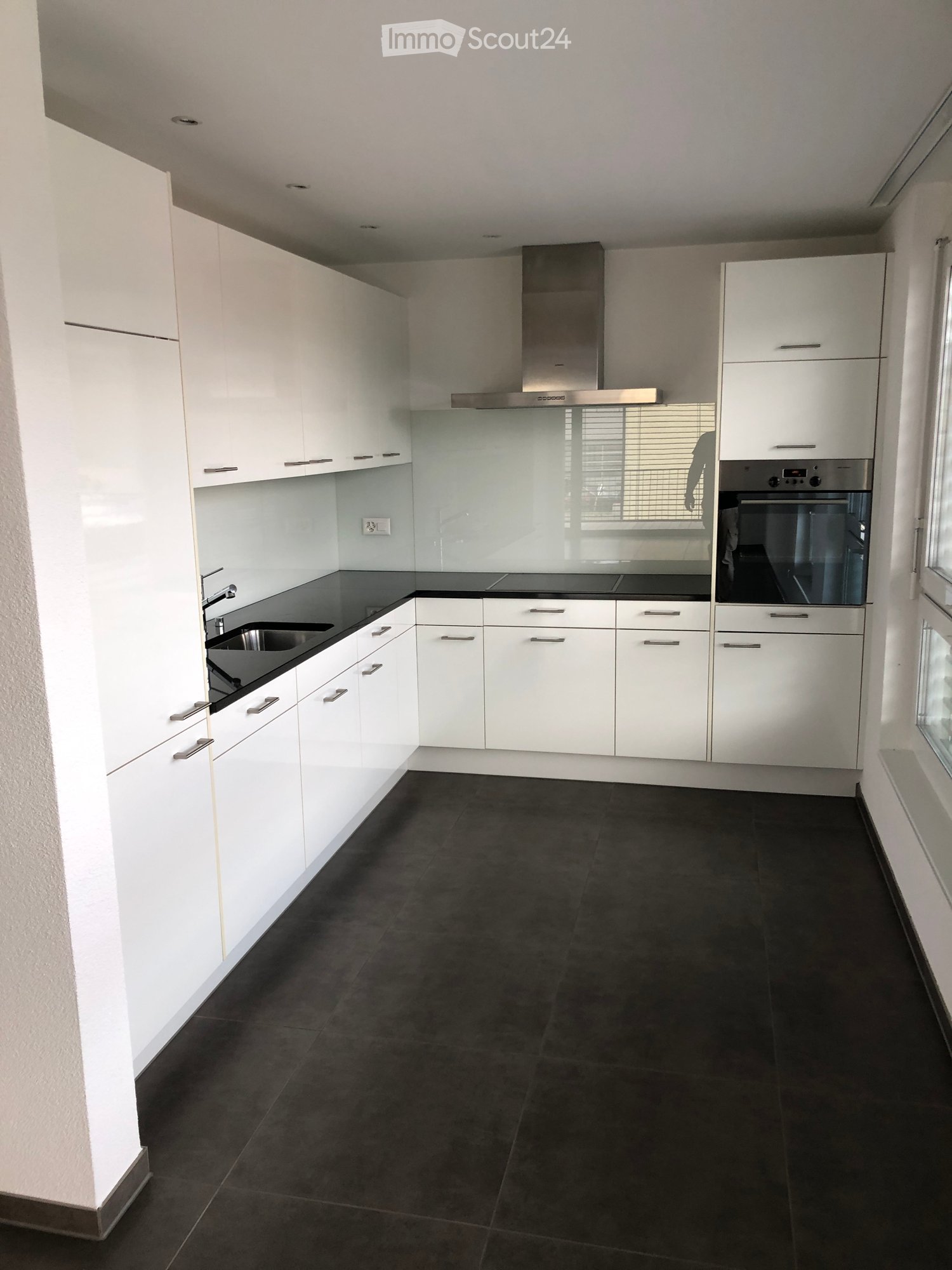 Modern kitchen with white cabinets, black countertops, stainless steel appliances, tiled floor, large windows, glass partition, power outlet.