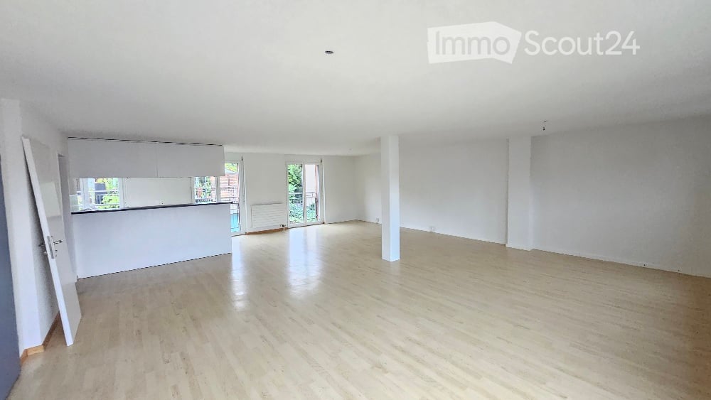large living room, hardwood floors, tall white columns, sliding glass doors, balcony, white kitchen island, white shelves