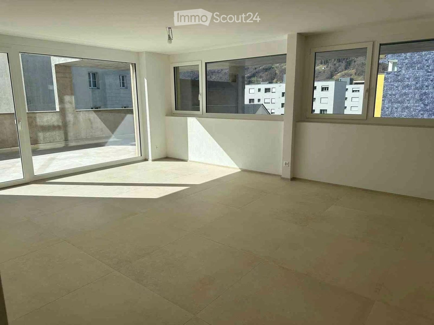 Empty room, sliding glass doors to balcony, large windows, beige tiles, mountain view