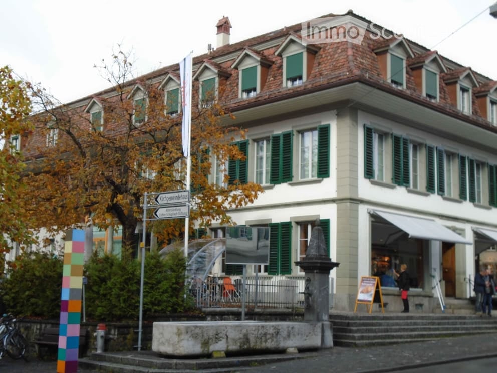 2 story house, red brick, green shutters, large windows, awning, street sign, trees, shrubs, bench