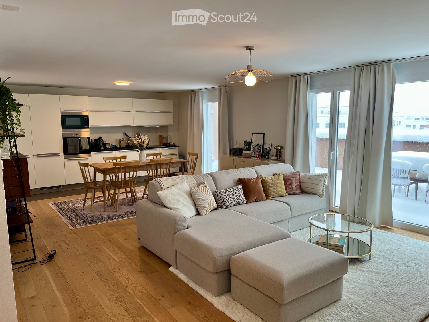 living room, gray sectional sofa, wooden dining table, kitchen, carpet, sliding glass doors, white curtains, large windows