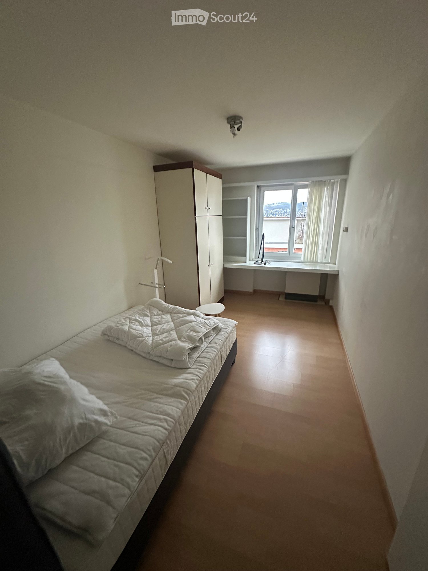 Single bed, two pillows, a blanket, wardrobe, desk, shelf, window with curtains