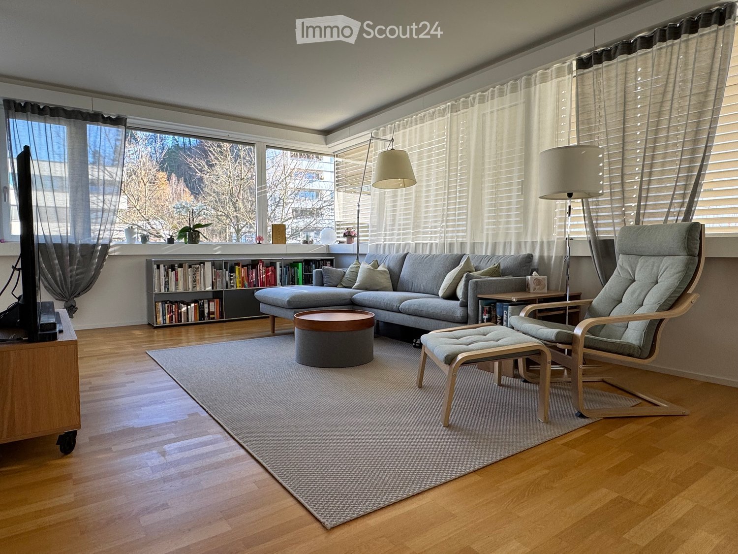 a L-shaped sofa, wooden coffee table, two armchairs, a small coffee table, floor lamp, TV on stand, bookcase, carpet