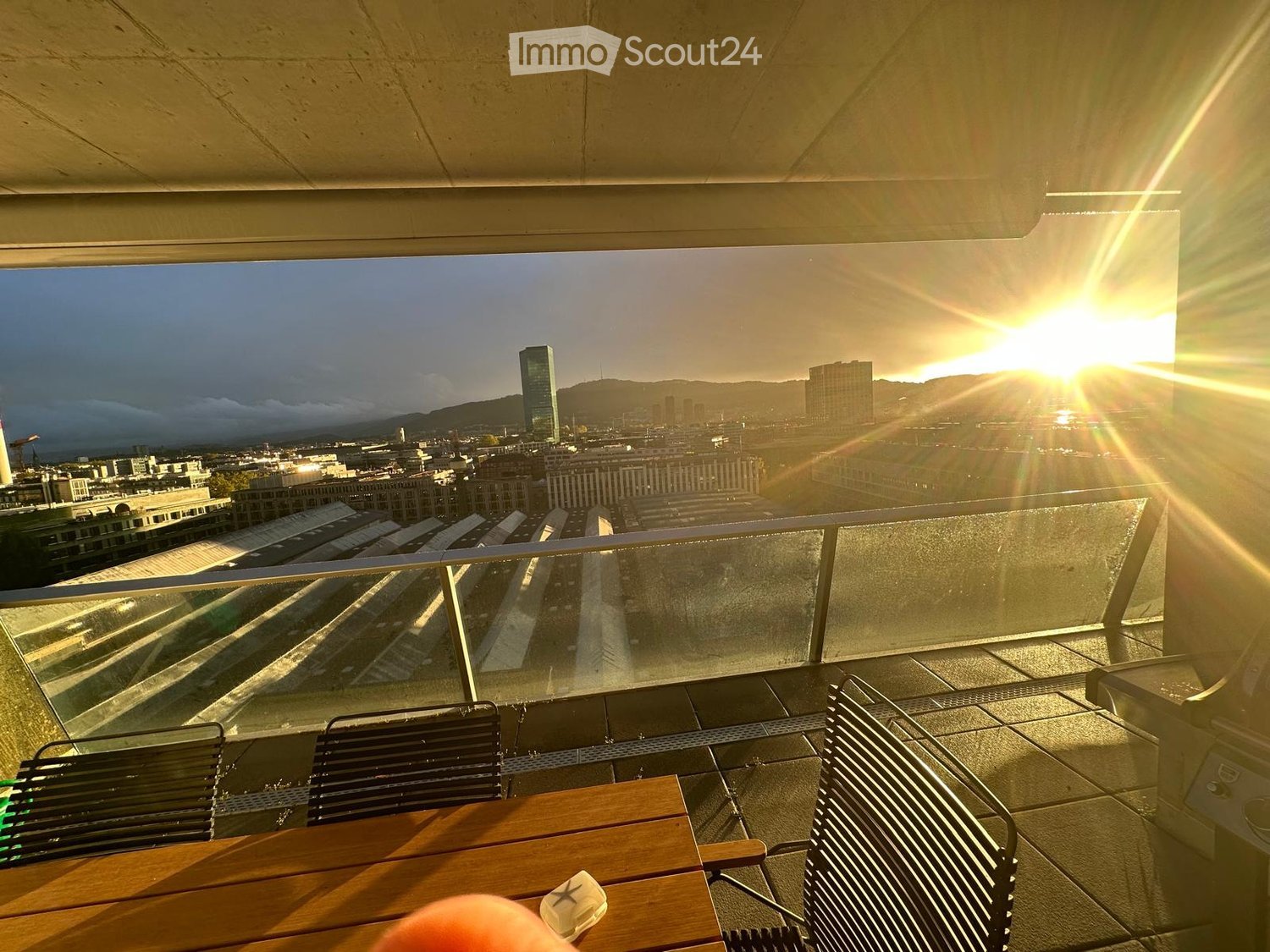 outdoor terrace with table and chairs, glass railing, stunning city view, warm sunlight