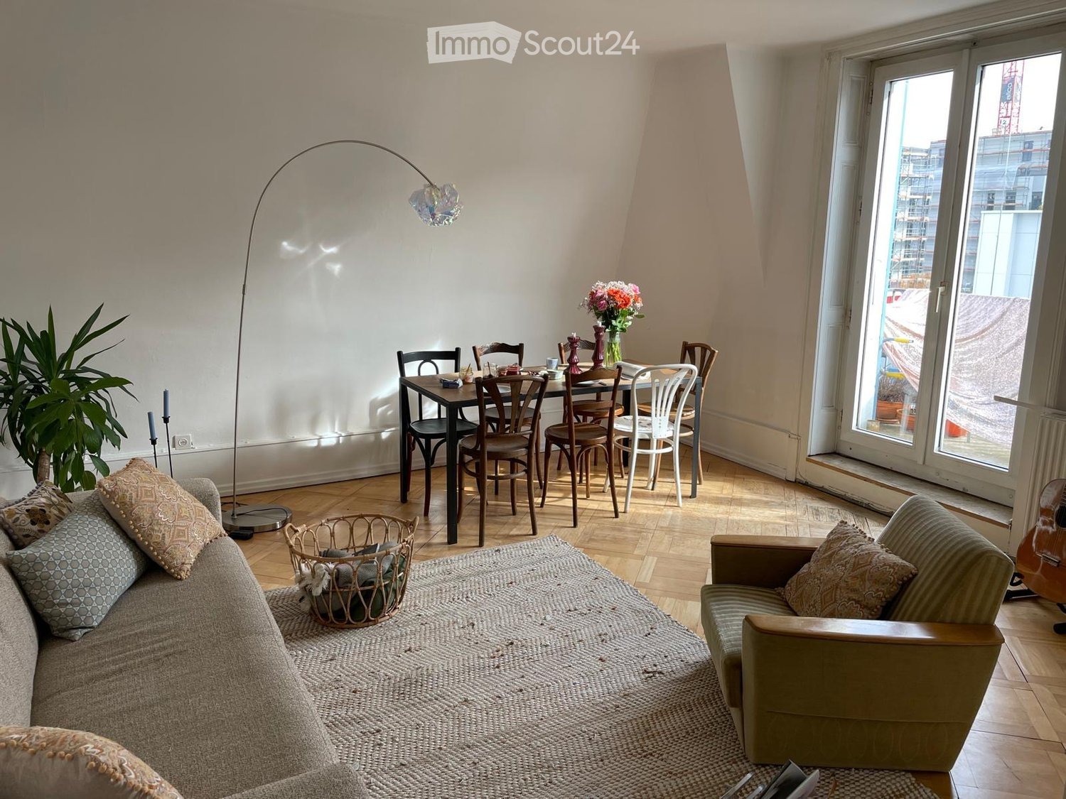 white walls, wooden floors, large windows, double doors, wooden table, chairs, sofa, lamp, basket, area rug, flowers, guitar