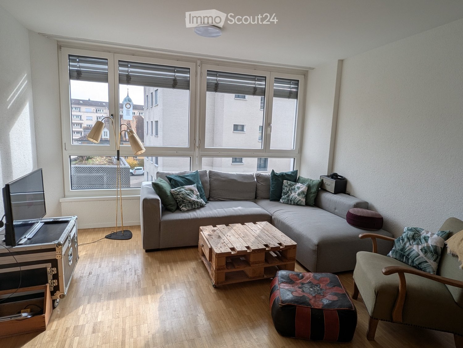 living room, gray couch, wooden coffee table, 3-way floor lamp, wooden floor, large windows, television