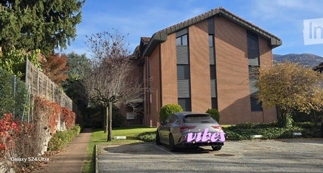 3-story building, brick wall, black windows, car parked in front, surrounded by trees and plants