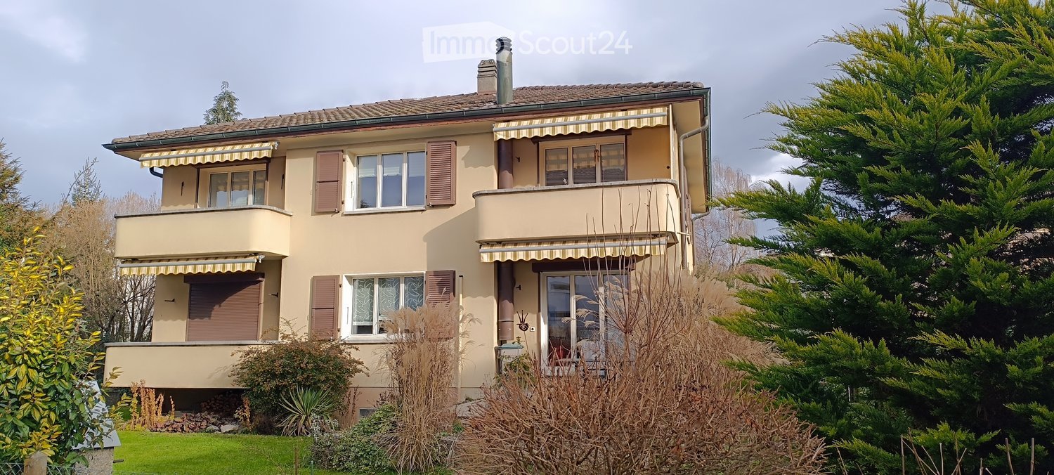 Two story house, beige color, wooden roof, two balconies, large garden