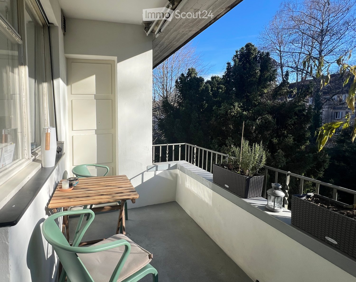 Wooden table, two green chairs, a white door, two potted plants, a lantern, a small cabinet, and a glass door