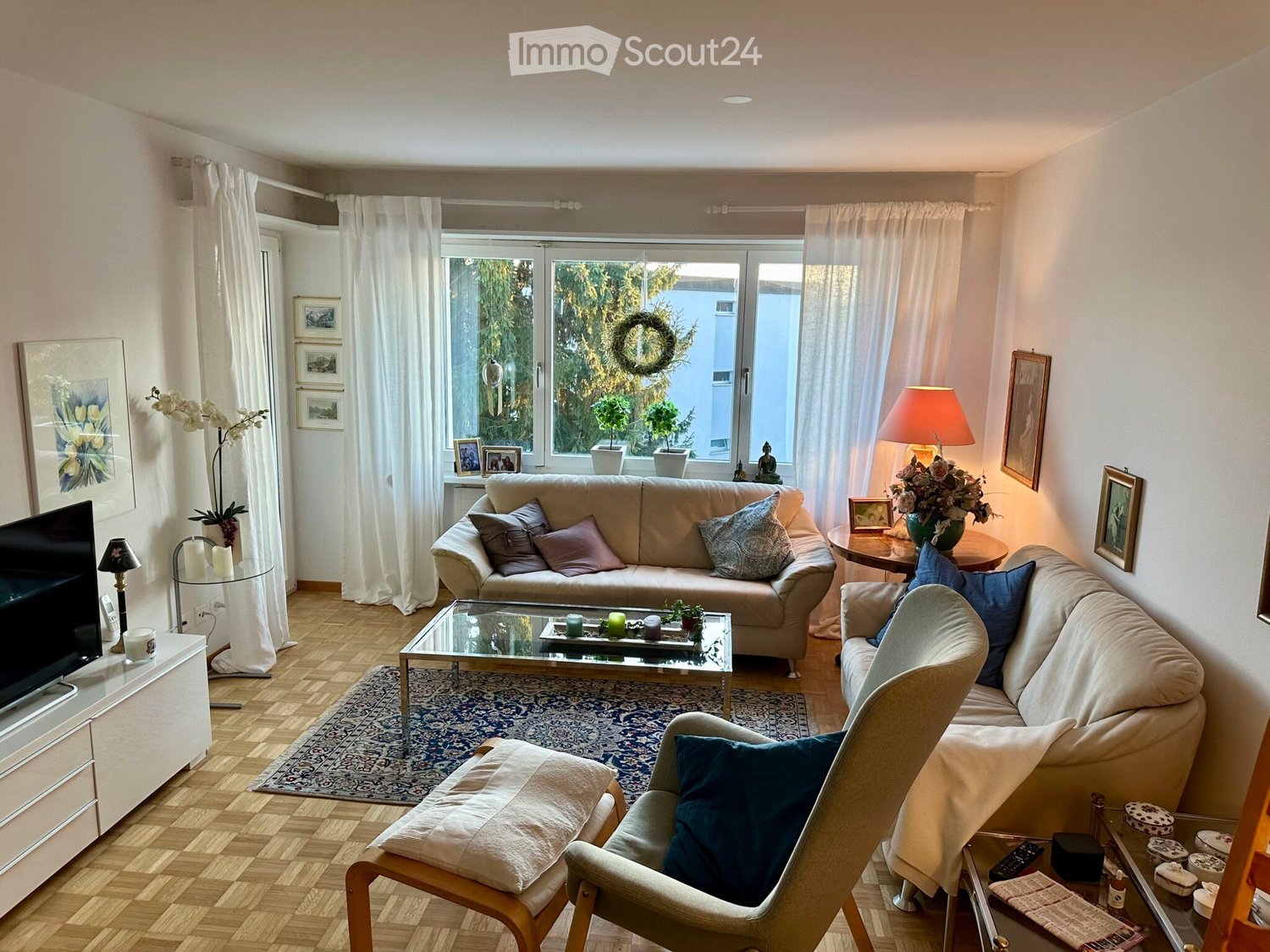 living room with beige couches, glass coffee table, rug, TV, pictures, plants, lamp, window, curtains