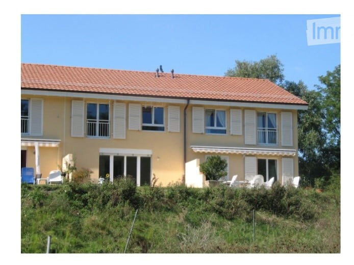 Yellow two-story house, with brown tiled roof, several large windows, and outdoor seating on front lawn