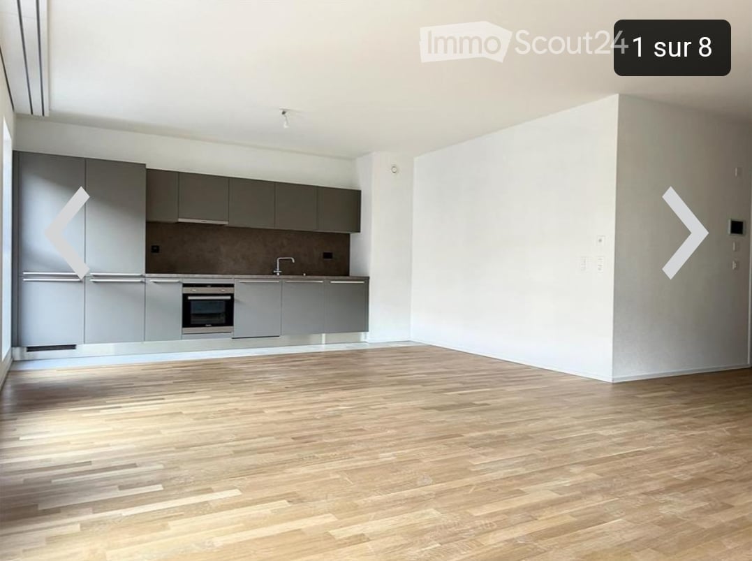 Open plan kitchen with oven and dishwasher, wooden floor, white walls, and gray cabinets.