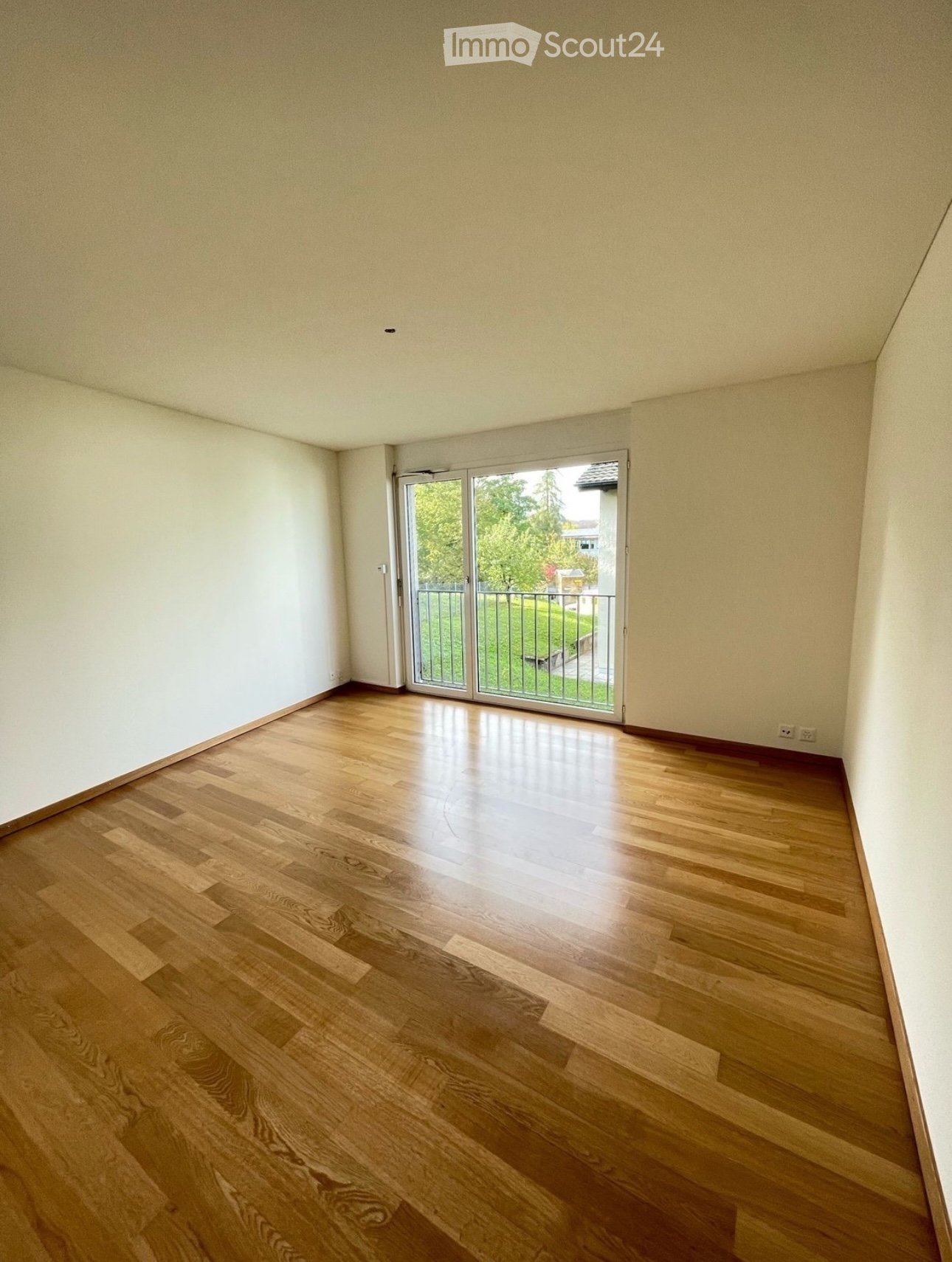 Empty room with wooden floor, white walls, sliding glass door, balcony with metal railing