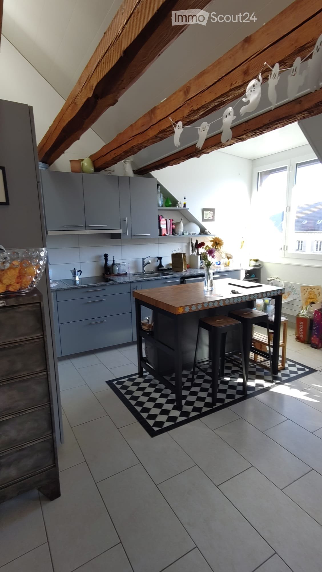 Kitchen with center island, gray cabinets, white tiled floor, wooden beams on ceiling