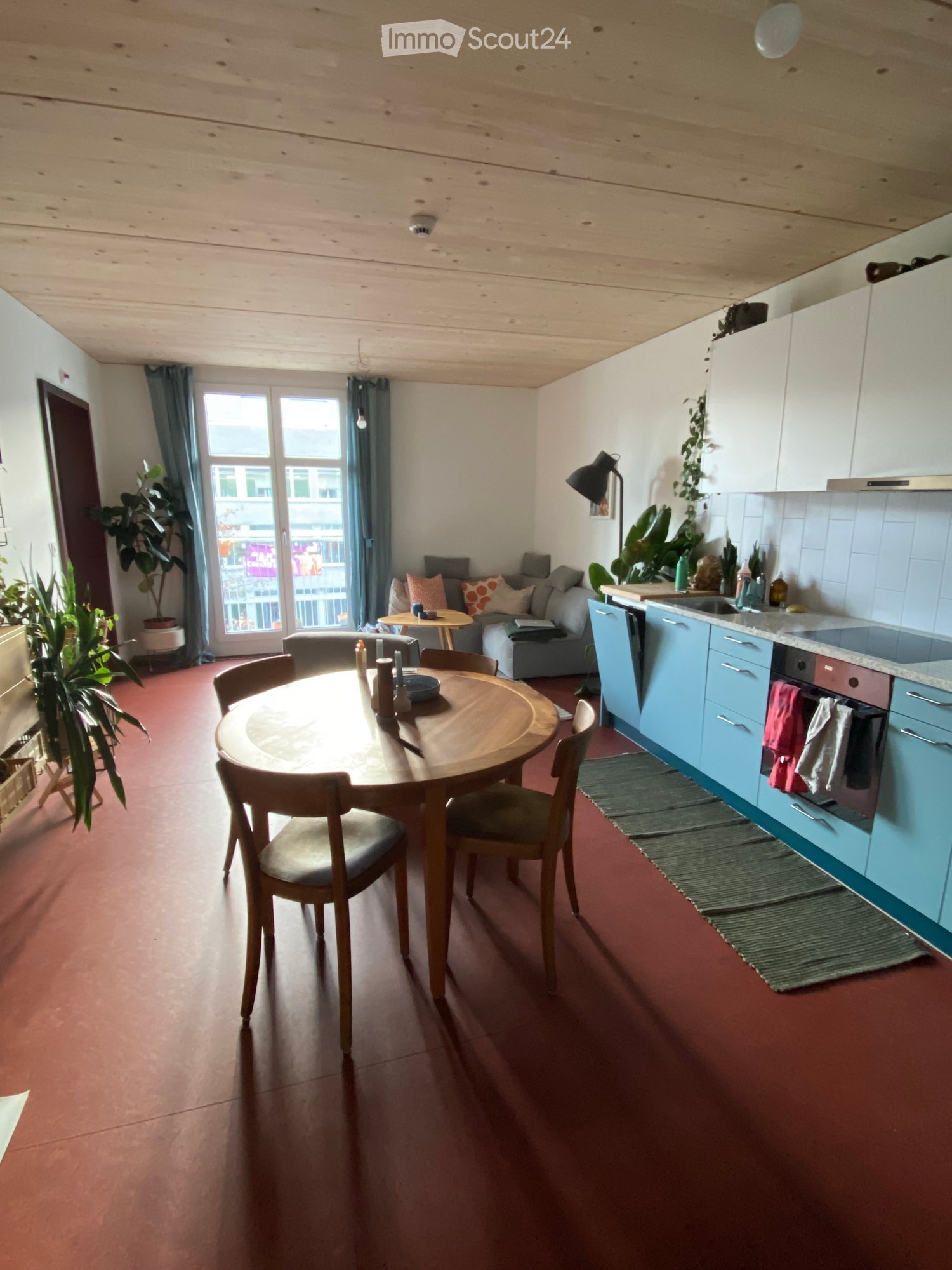 round wooden table with chairs, blue cupboards, sink, stove, lamp, couch, plant