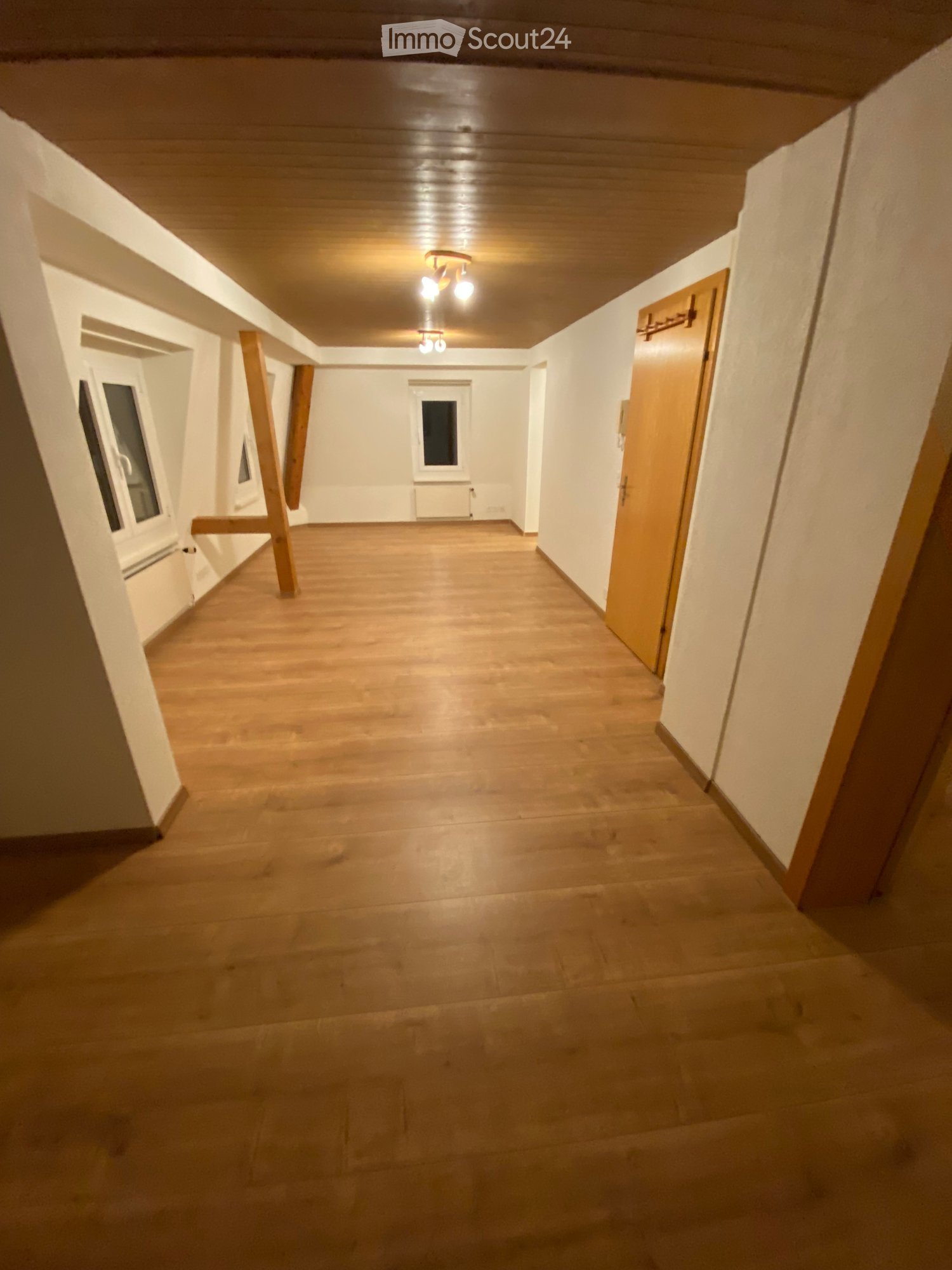 large empty room, hardwood floor, white walls, exposed wooden beams, three windows