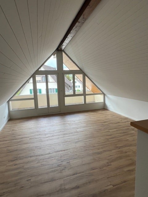 Atrium attic room, hardwood floors, white walls, large windows, slanted ceiling