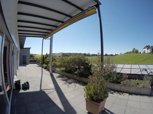 A covered terrace with retractable canopy, surrounded by greenery, offering a view of the surrounding landscape.