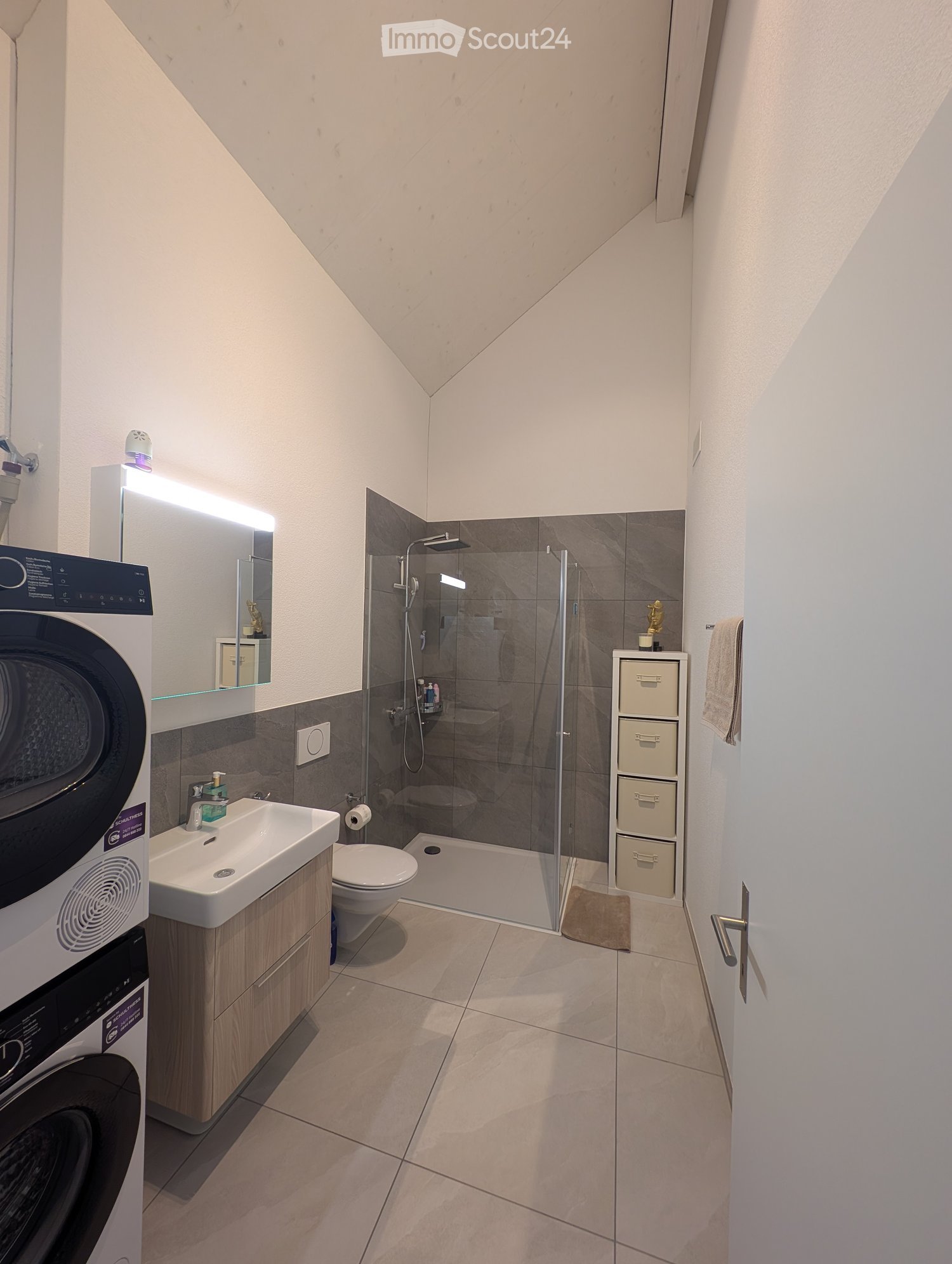 Modern white tiled bathroom with toilet, sink, shower, and built-in washing machine.