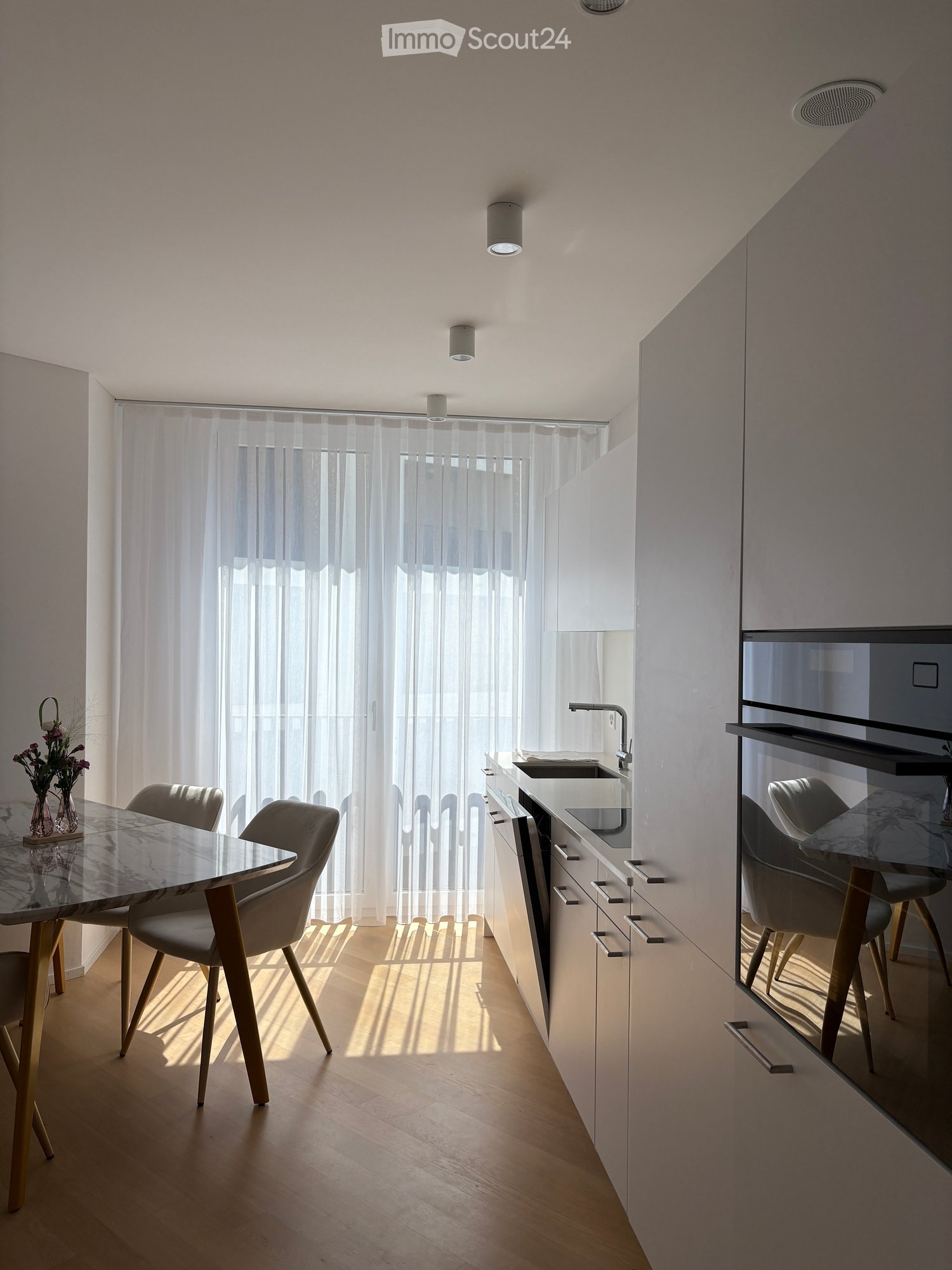 Open kitchen, table and chairs, modern fixtures, window with curtains