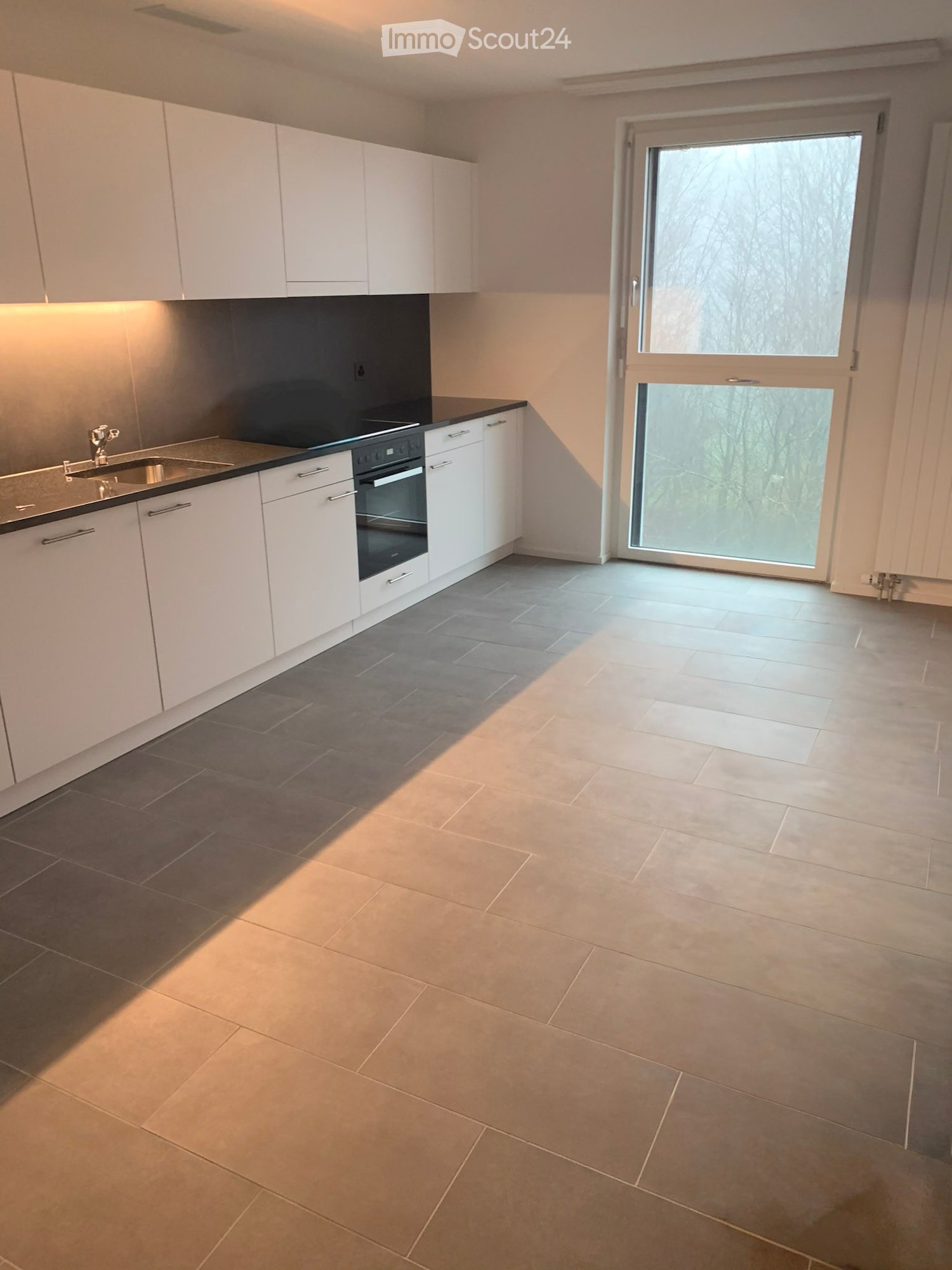 Kitchen with appliances and cabinets, window with outdoor view, tiled floor.