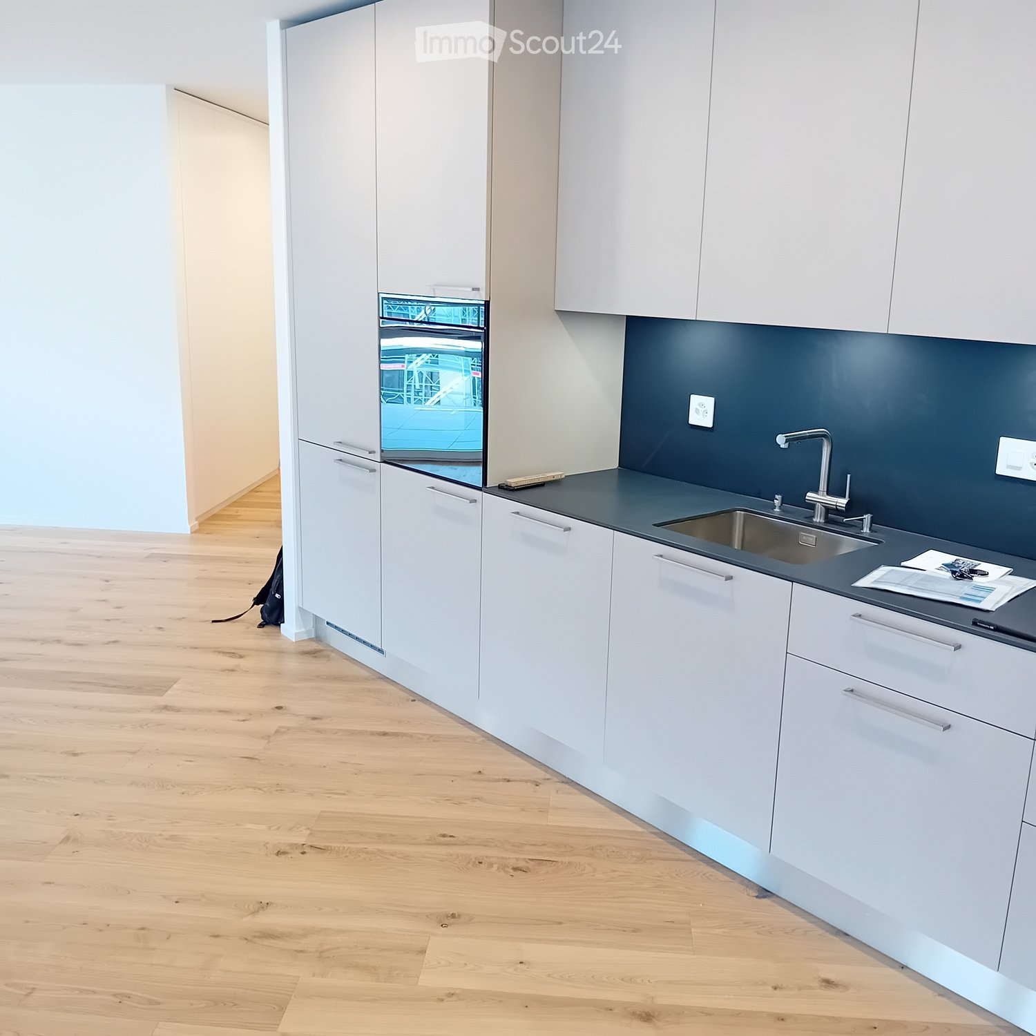Modern kitchen with white cabinets, dark countertops, and a stainless steel sink. Wooden flooring and a small oven are visible.