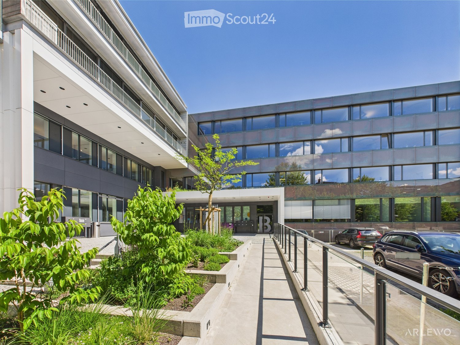 Modern office building with glass windows, landscaped entrance, and parking area.