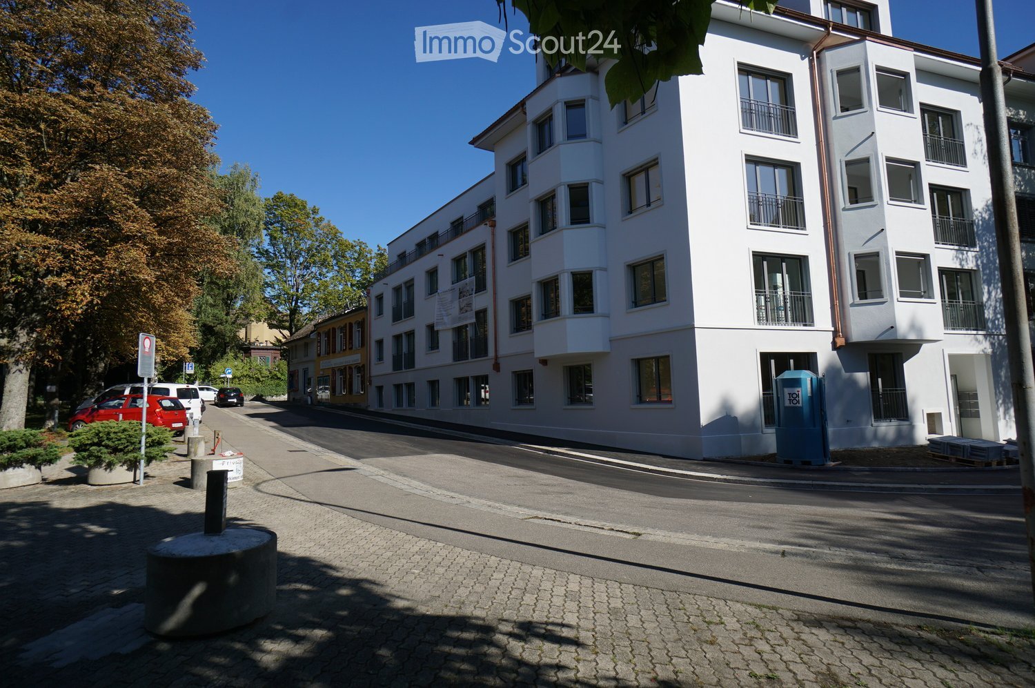 White residential building, multiple balconies, street parking