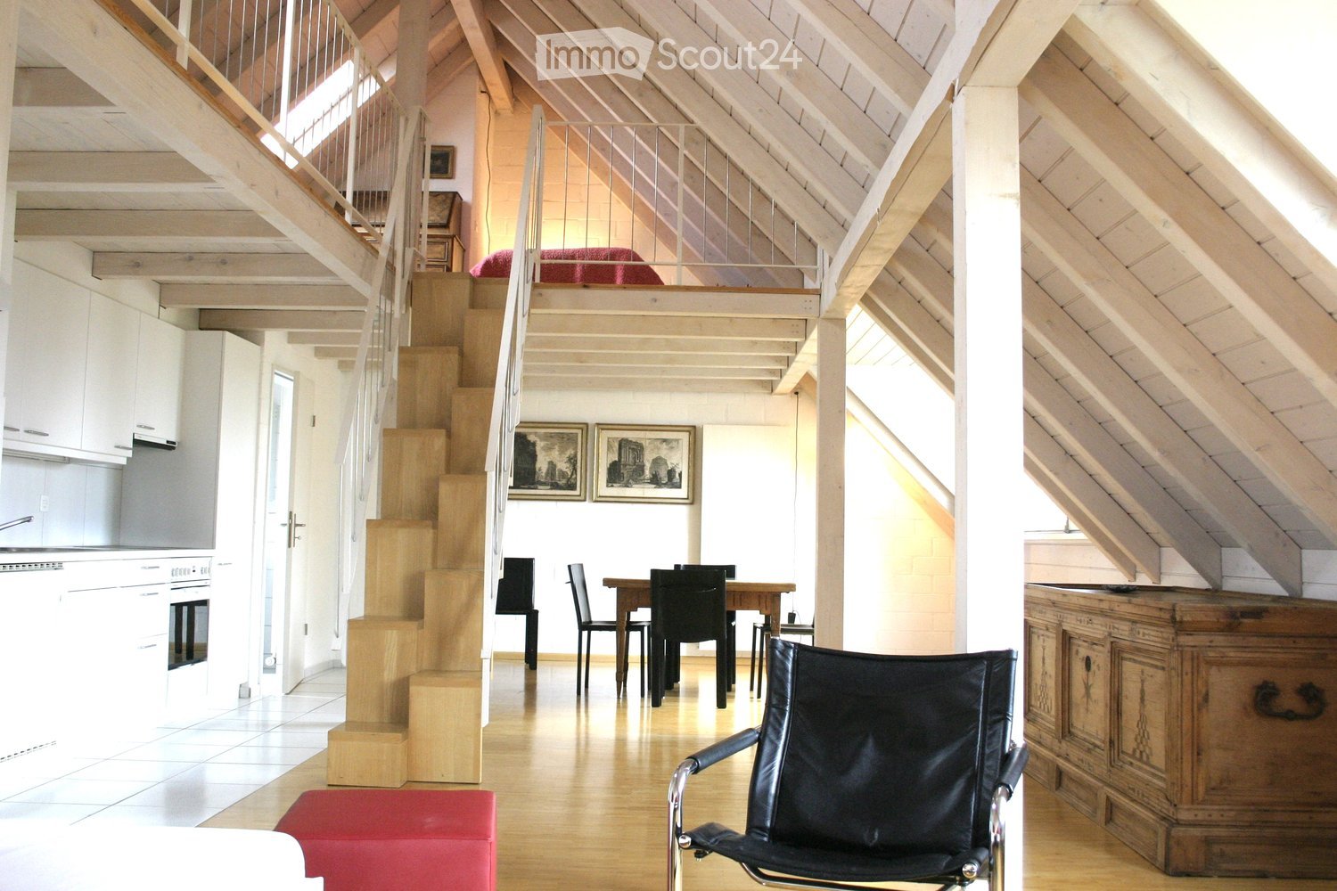 loft area with staircase, dining area, black leather chair, wooden dining table, white kitchen cabinets, red cushion on floor, picture frames on wall