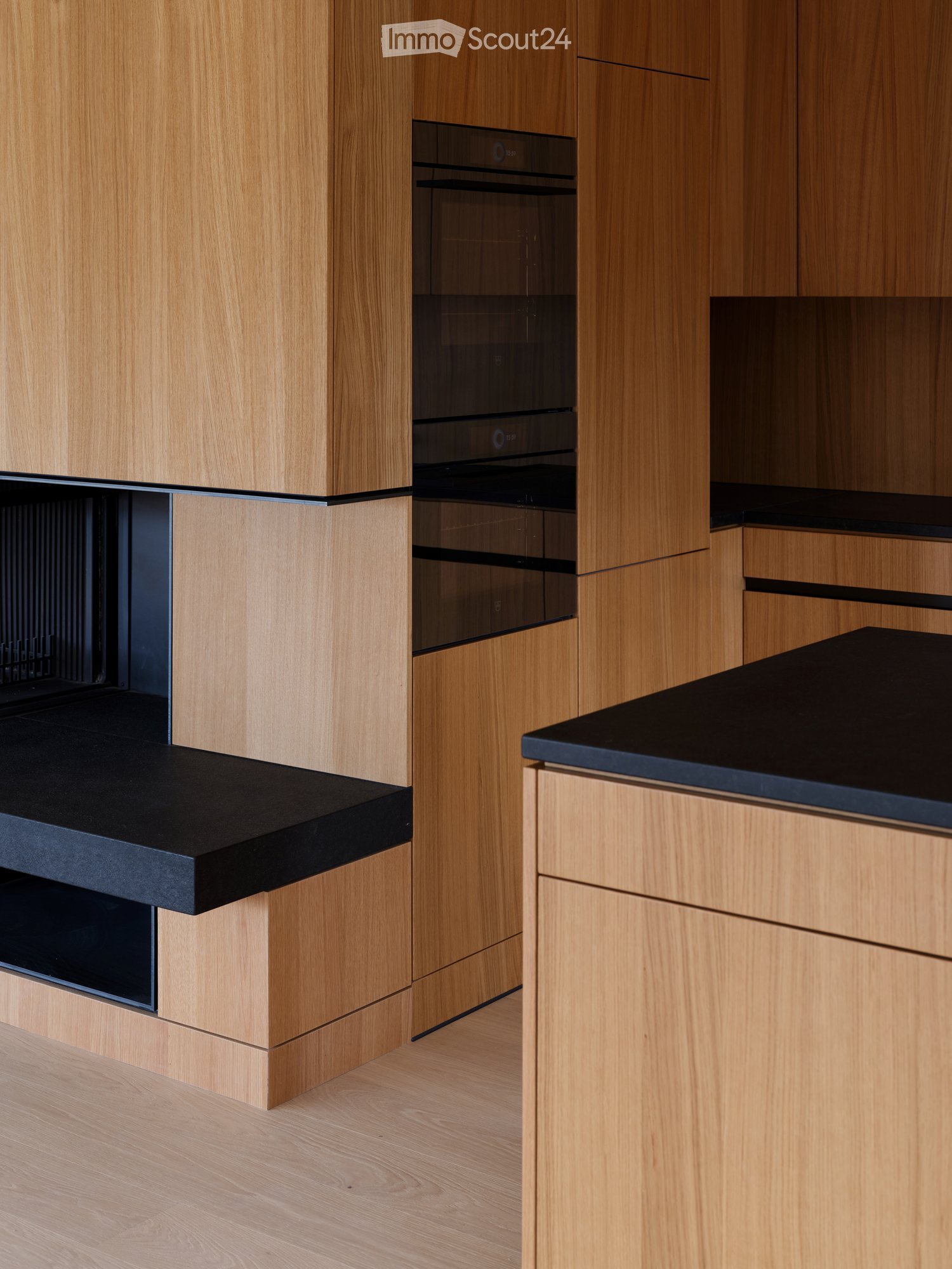 Modern kitchen with light wooden cabinets, black countertops, and built-in oven.