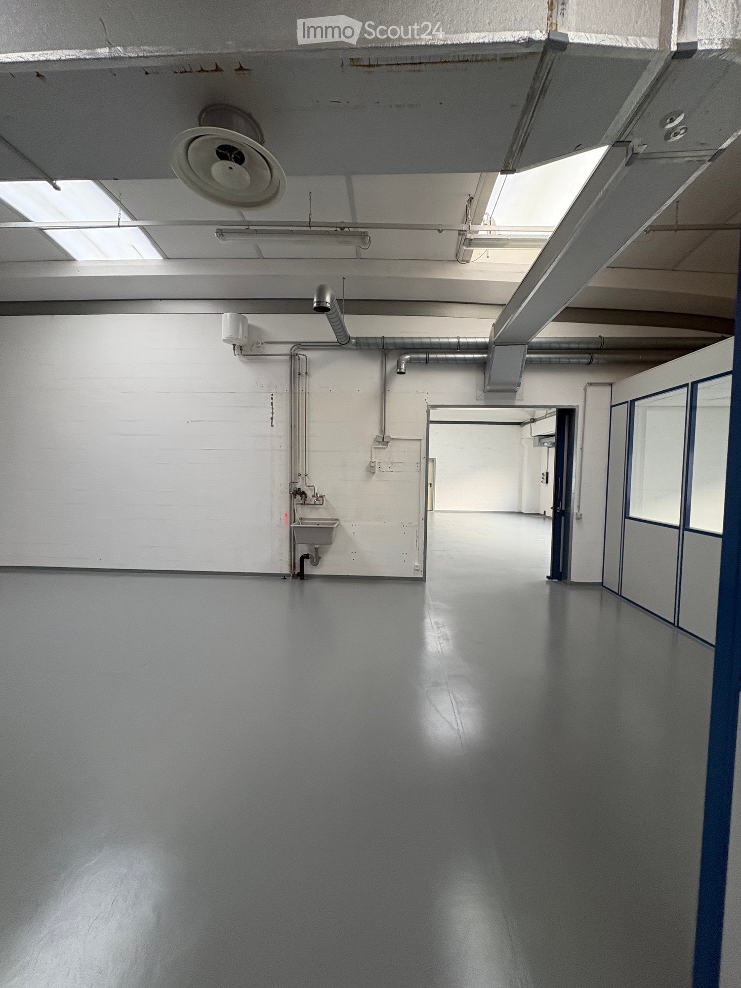Empty room with white walls, gray floor, a sink, and pipes on the wall