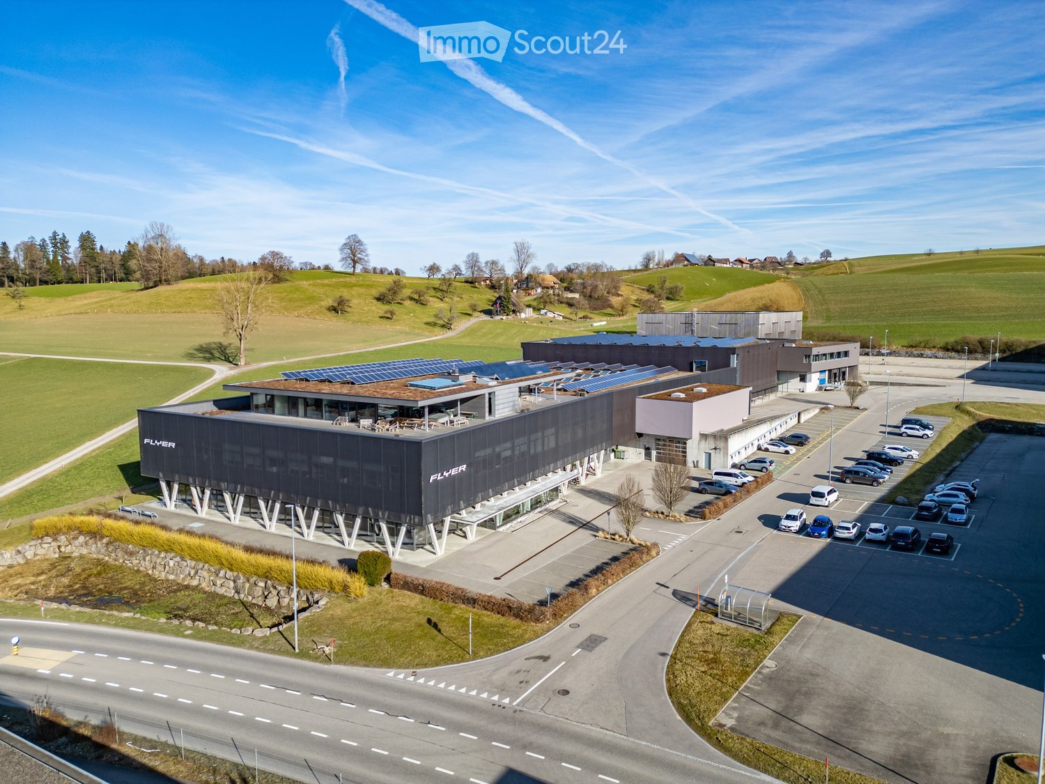 modern building with solar panels, large parking lot, surrounded by green fields