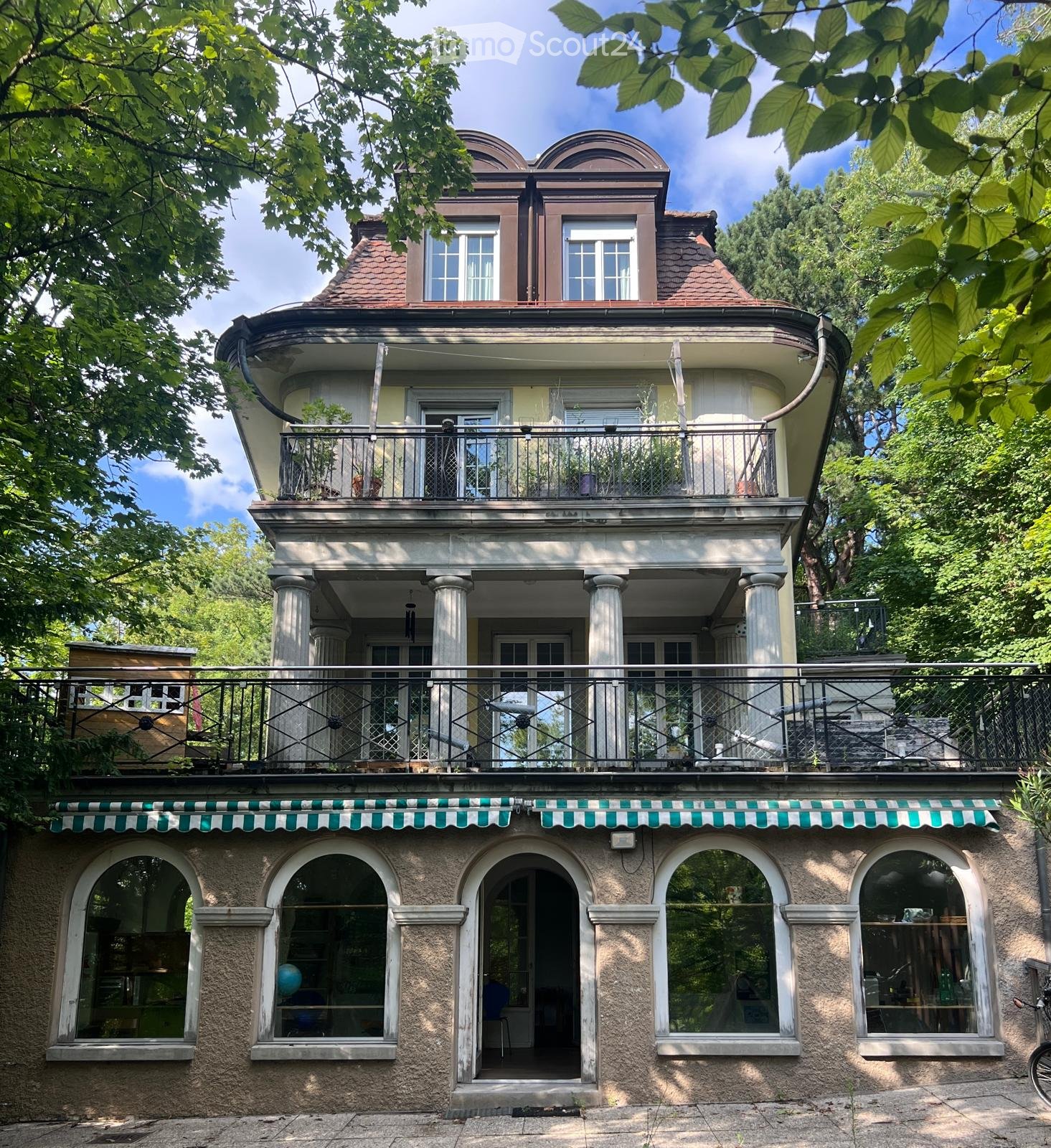 2 story house, yellow and brown facade, arched windows, balcony, green awning