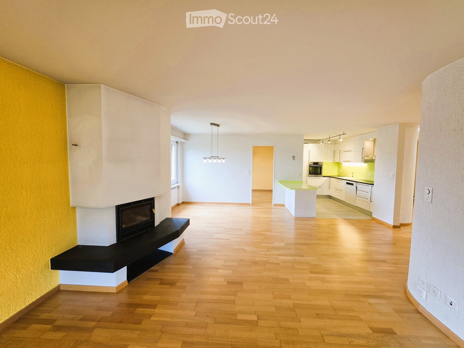 Bright hallway with wooden flooring, modern fireplace on the left, and a kitchen area visible at the end.