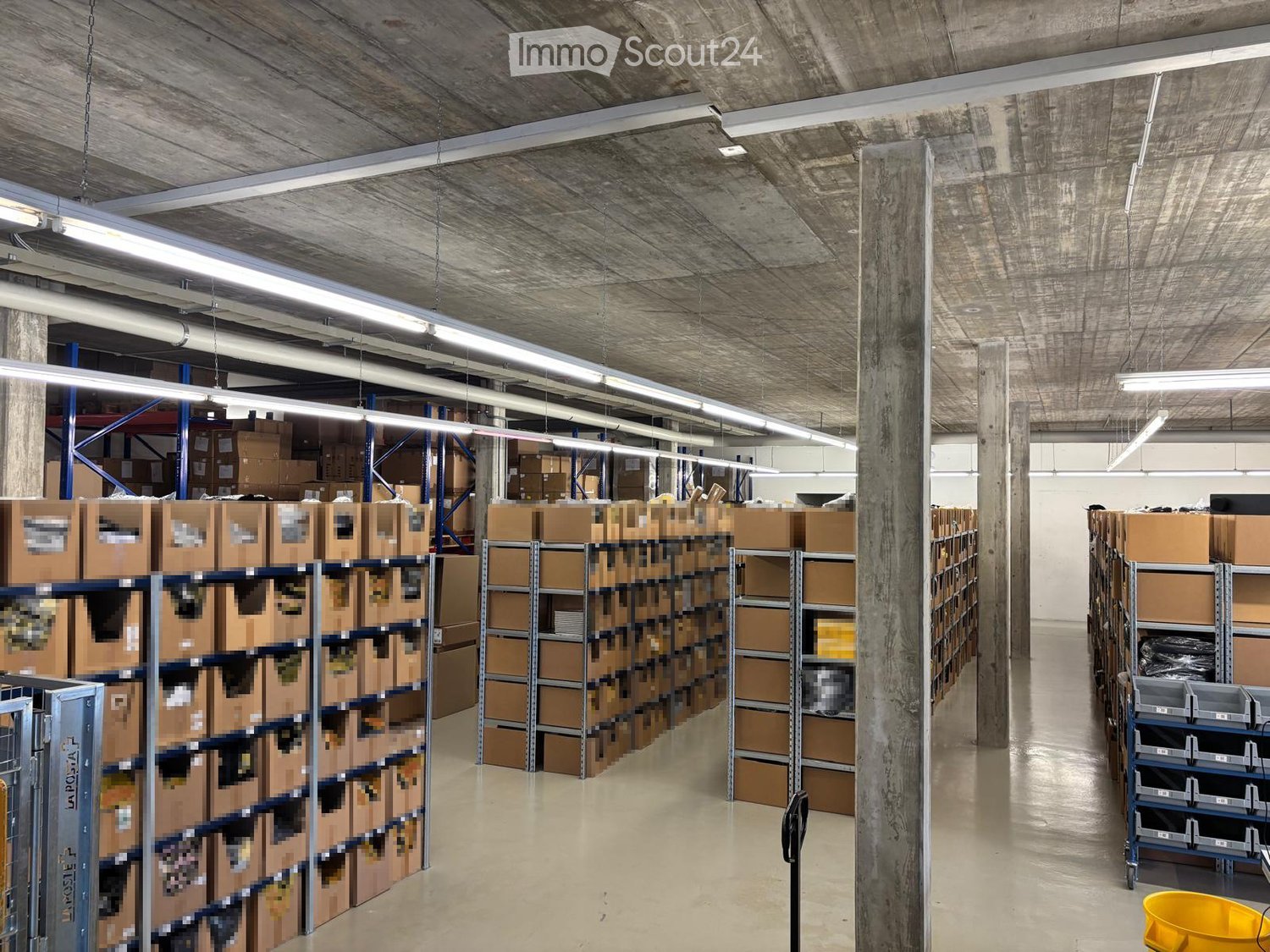Warehouse with multiple rows of storage boxes, metal shelves, and fluorescent lighting.