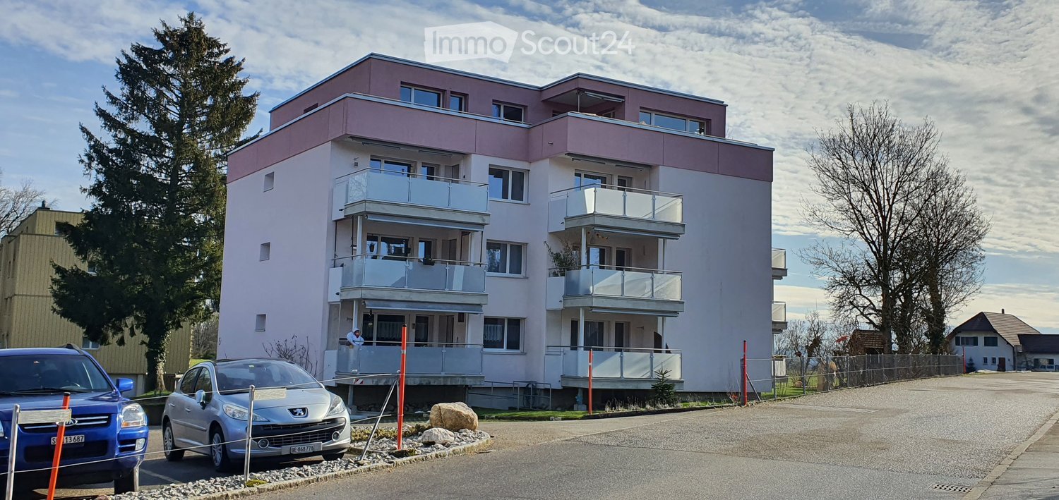 3 story apartment building, pink and white paint, windows, balconies, cars parked in front