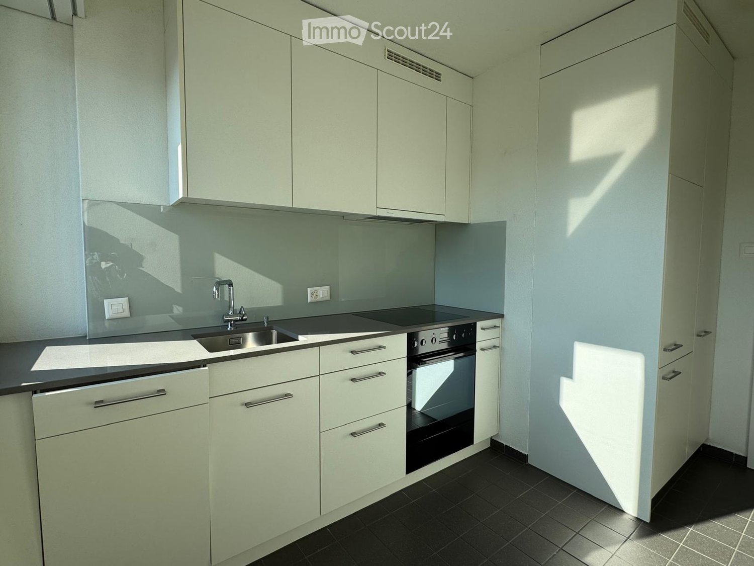 modern kitchen with white cabinets, black countertops, stainless steel sink, built-in oven, dishwasher, and washing machine