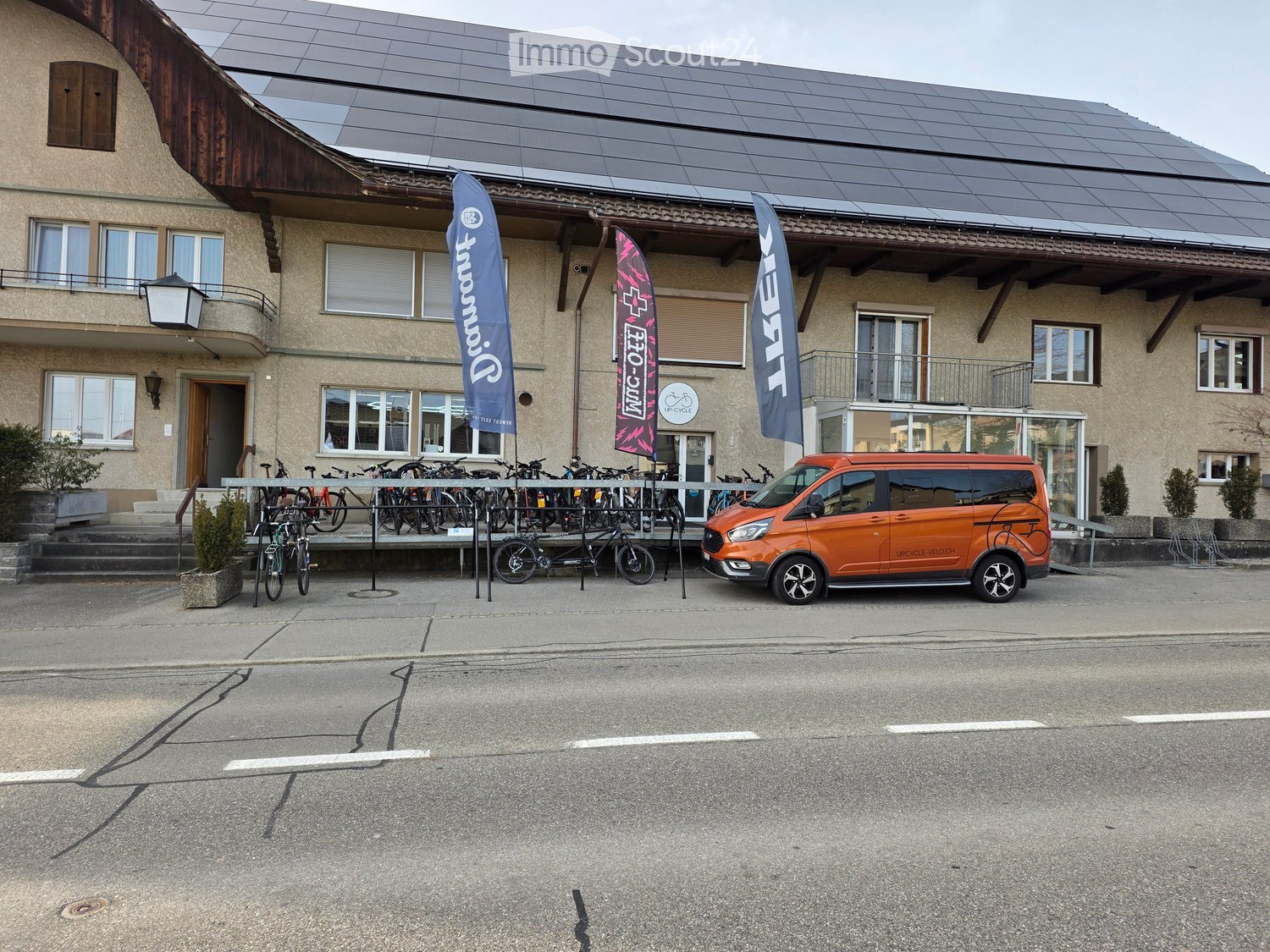 Building with solar panels, bicycles parked in front, orange van parked in front