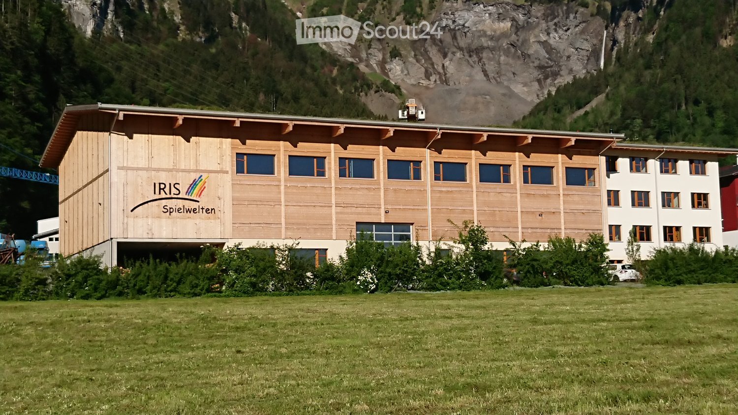 Two story wooden building, lots of windows, text on the side: 'IRIS Spielwelten', car parked in front