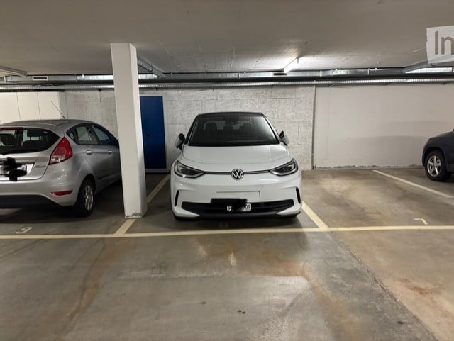 underground parking lot with three cars parked, white walls, yellow markings