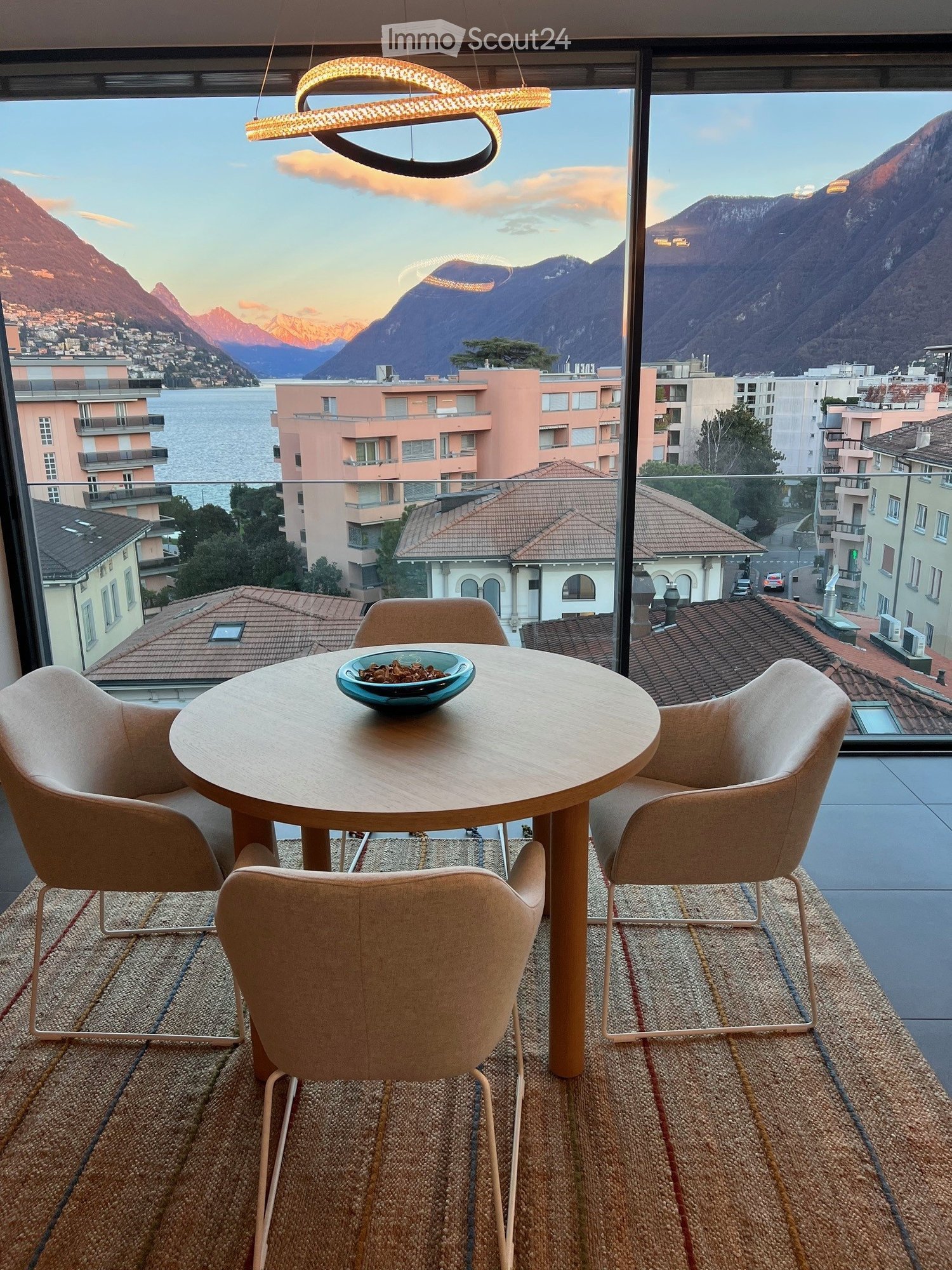 Dining table, chairs, bowl, hanging light, large windows, rug, city view, mountains