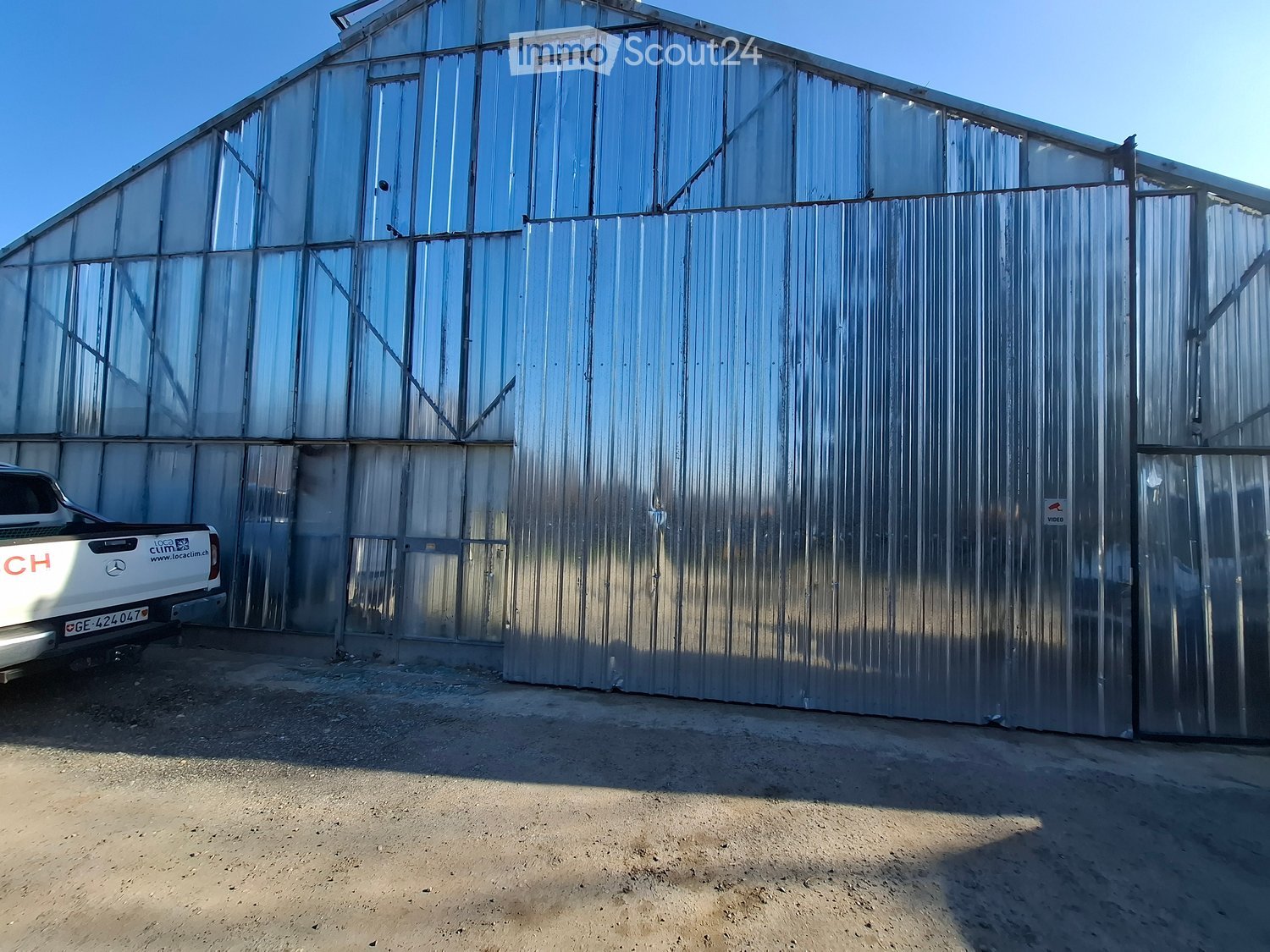 Large metal building with glass windows, open door, white pickup truck parked in front